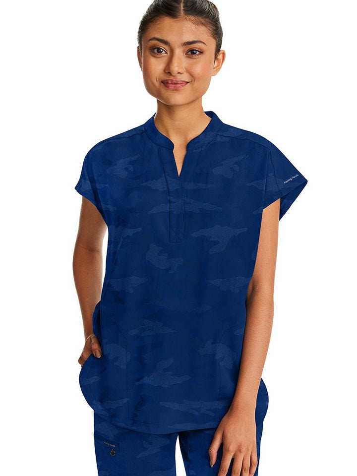 A young female Nurse Practitioner wearing a Products Purple Label Women's Journey Camo Top in Navy size Small featuring a modern fit.