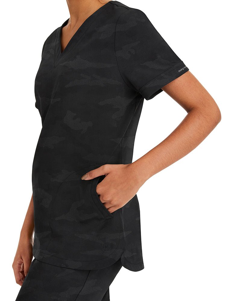 Female nurse wearing a Purple Label Women's Joy Camo Top in black featuring 1 cell phone pocket.
