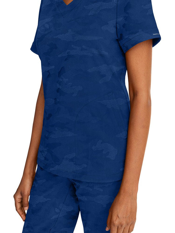 Young nurse wearing a Purple Label Women's Joy Camo Top in Navy with 2 welt pockets on each side.