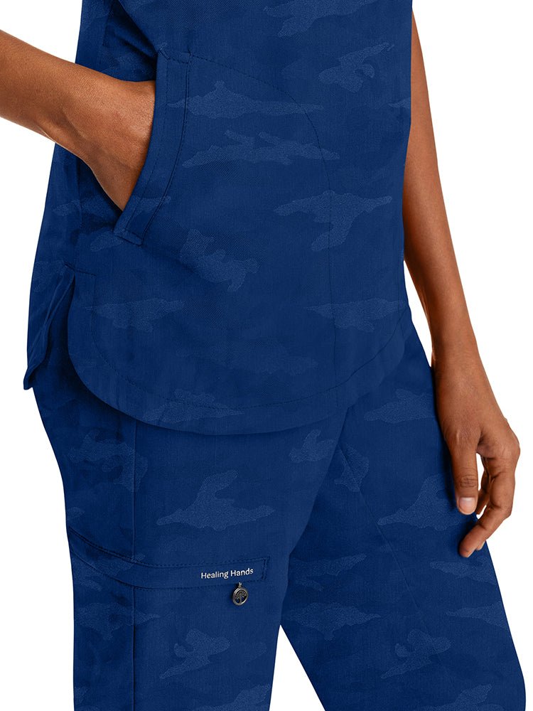 Young nurse wearing a Purple Label Women's Joy Camo Top in Navy with 2 welt pockets on each side.