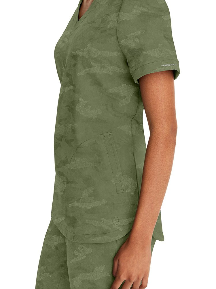 Young nurse wearing a Purple Label Women's Joy Camo Top in Olive with 2 welt pockets on each side.