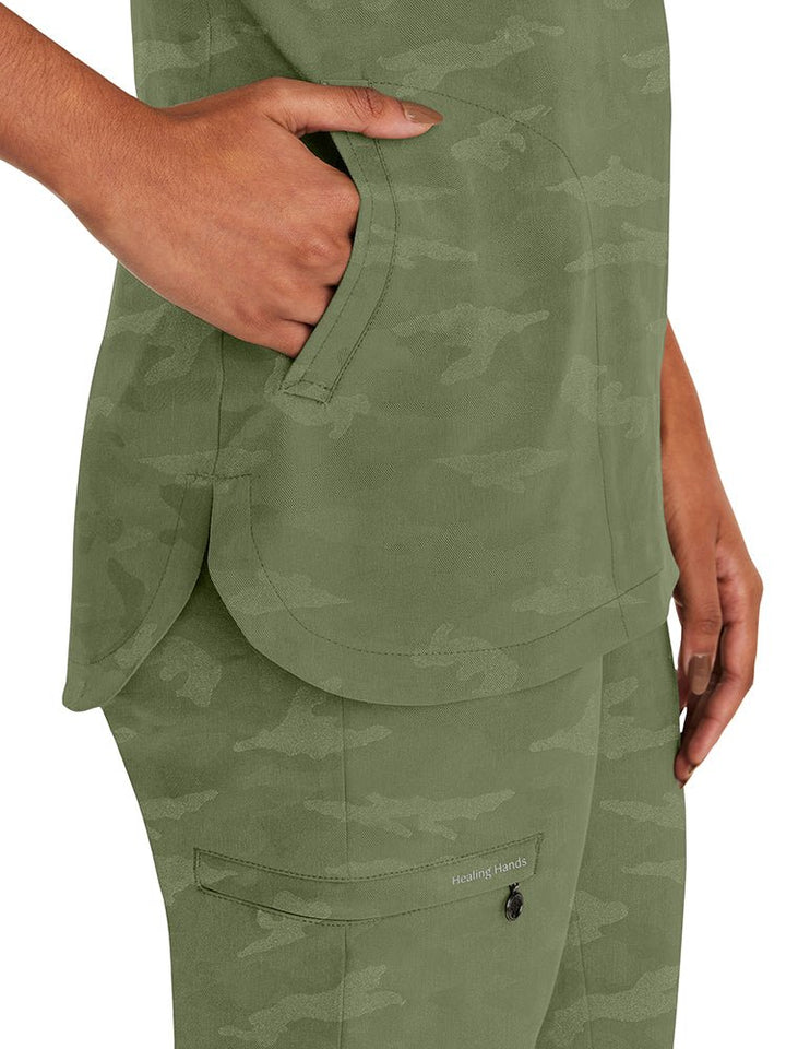 Young nurse wearing a Purple Label Women's Joy Camo Top in Olive with 2 welt pockets on each side.