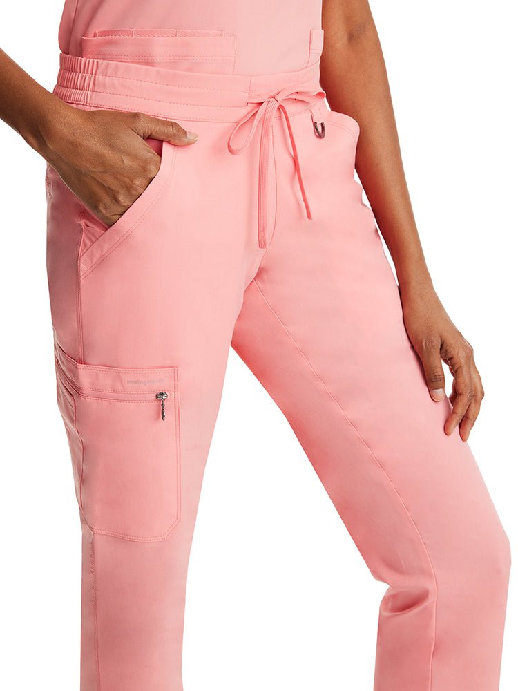 Young woman wearing a pair of Purple Label Women's Tamara Cargo Scrub Pants in "Melon" featuring 2 front slash pockets.