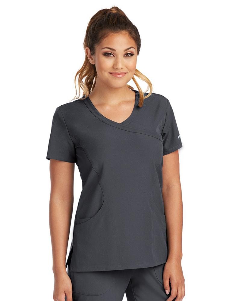 A female LPN wearing a Skechers Women's Reliance Mock Wrap Scrub Top in Pewter size medium featuring front princess seaming & topstitching detail throughout.