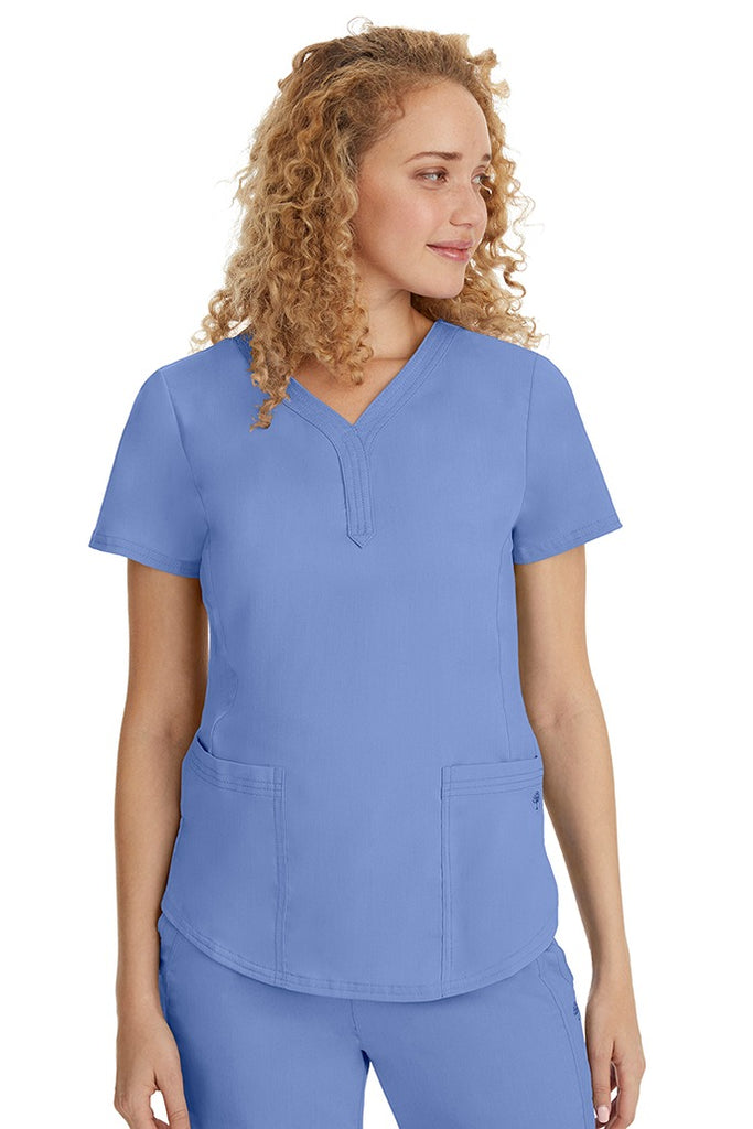 A young female healthcare professional wearing a Purple Label Women's Jane V-Neck Scrub Top in Ceil featuring 2 front patch pockets.