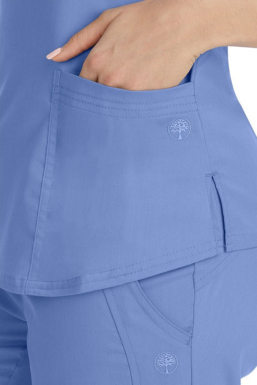 A female healthcare worker wearing a Purple Label Women's Jane V-Neck Scrub Top in Ceil featuring triple needle stitch detail at the pockets.