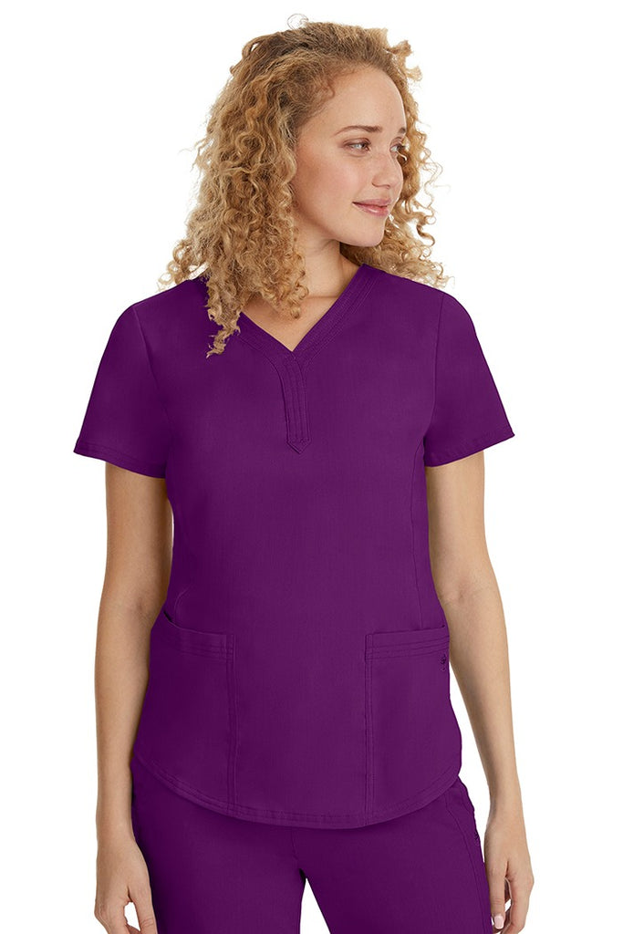 A young female healthcare professional wearing a Purple Label Women's Jane V-Neck Scrub Top in Eggplant featuring 2 front patch pockets.