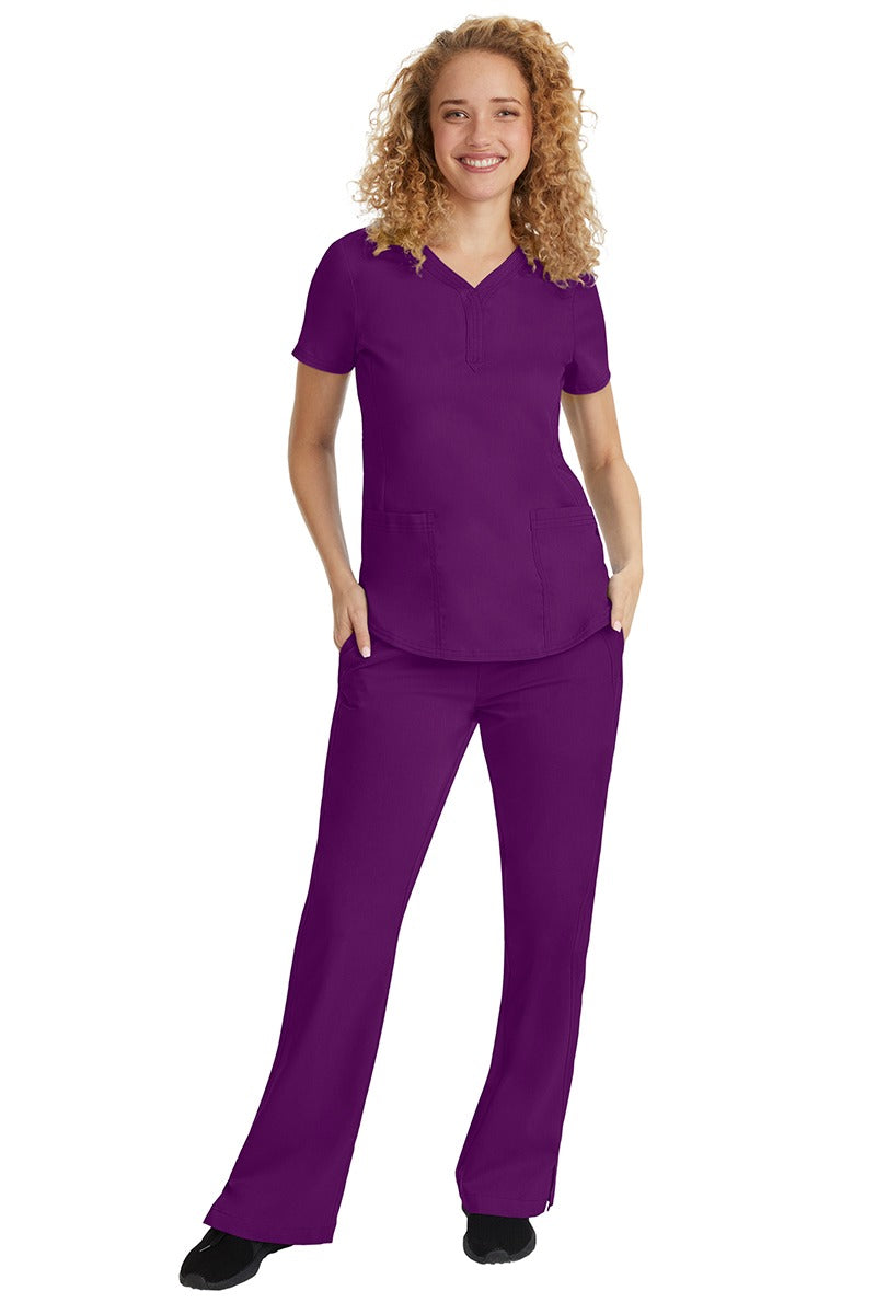 A young female nurse wearing a Purple Label Women's Jane V-Neck Scrub Top in Eggplant featuring a V-neckline & short sleeves.
