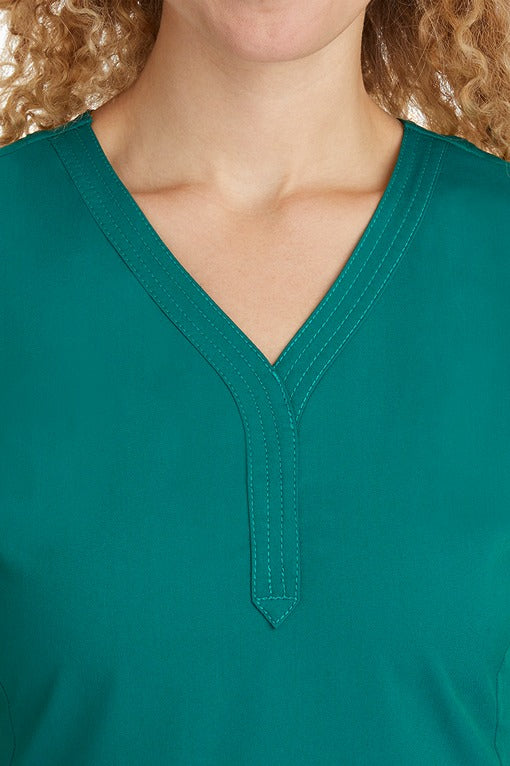 A young woman CNA wearing a Women's Jane V-Neck Scrub Top from Purple Label by Healing Hands in Hunter Green featuring triple stitch detail at the neckline.