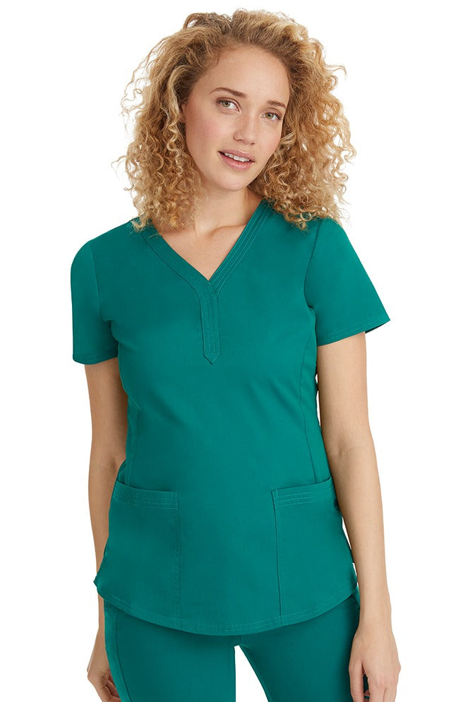 A young female healthcare professional wearing a Purple Label Women's Jane V-Neck Scrub Top in Hunter Green featuring 2 front patch pockets.