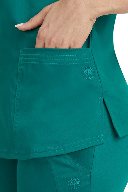 A female healthcare worker wearing a Purple Label Women's Jane V-Neck Scrub Top in Hunter Green featuring triple needle stitch detail at the pockets.