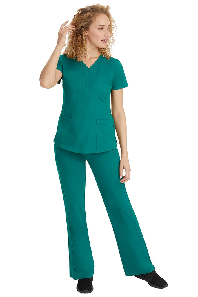 A young female nurse wearing a Purple Label Women's Jane V-Neck Scrub Top in Hunter Green featuring a V-neckline & short sleeves.