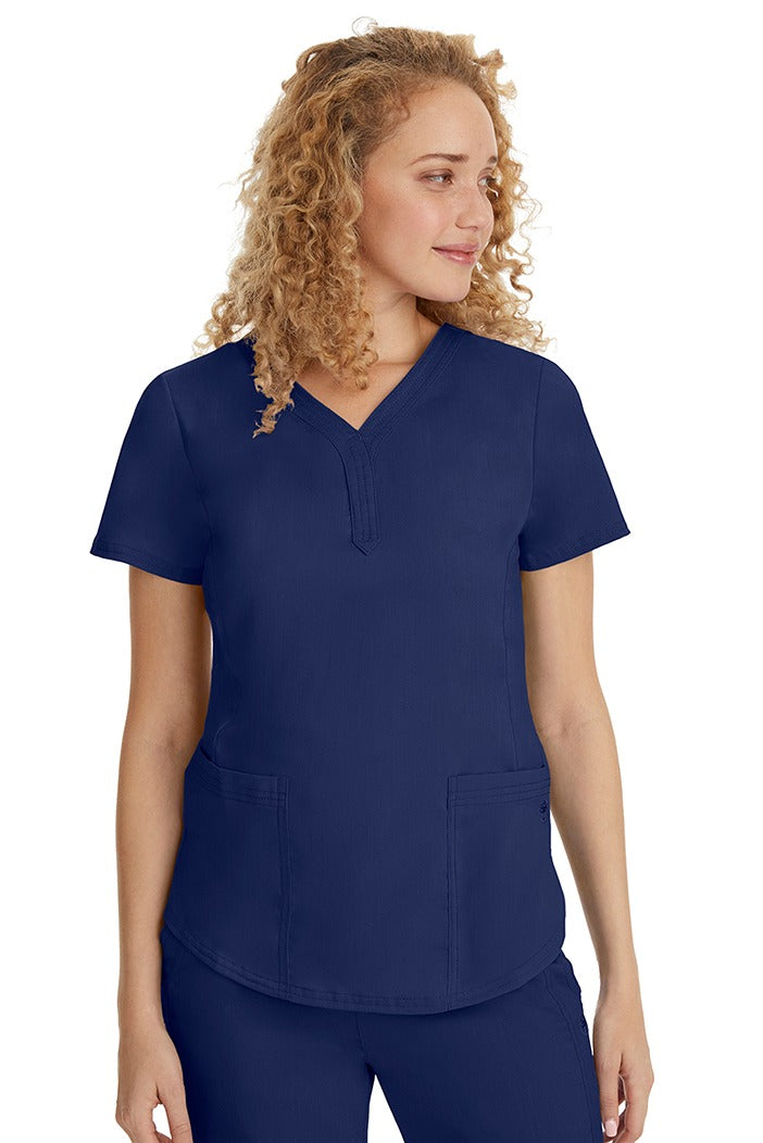 A young female healthcare professional wearing a Purple Label Women's Jane V-Neck Scrub Top in Navy featuring 2 front patch pockets.