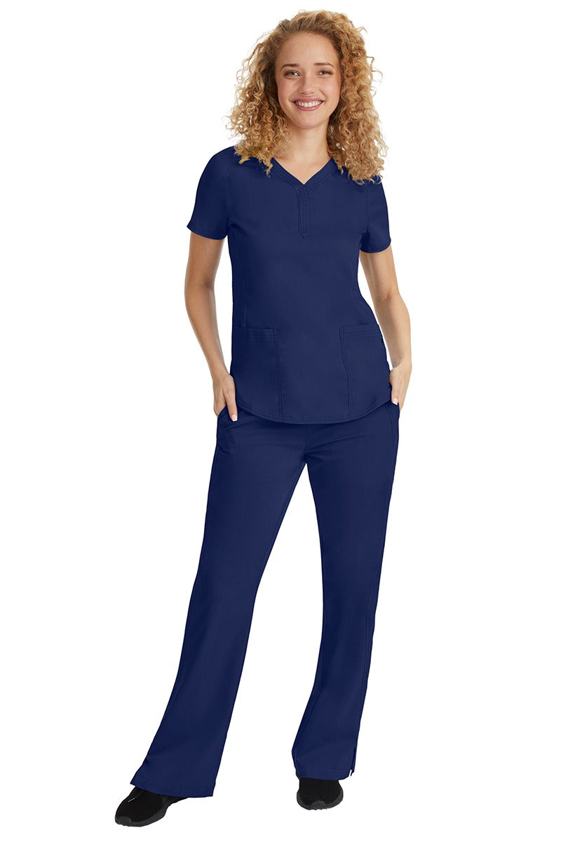 A young female nurse wearing a Purple Label Women's Jane V-Neck Scrub Top in Navy featuring a V-neckline & short sleeves.