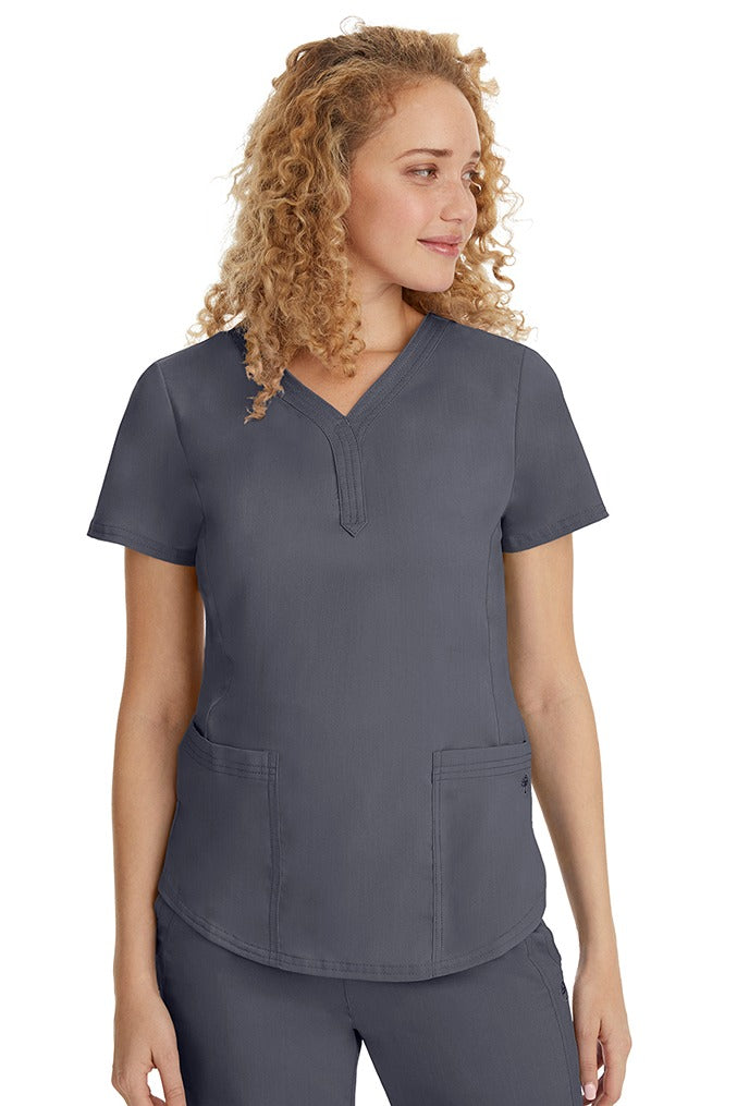 A young female healthcare professional wearing a Purple Label Women's Jane V-Neck Scrub Top in Pewter featuring 2 front patch pockets.