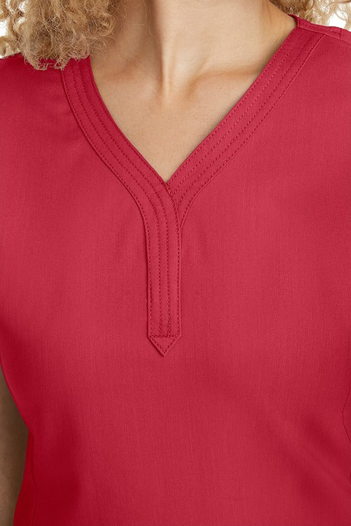 A young woman CNA wearing a Women's Jane V-Neck Scrub Top from Purple Label by Healing Hands in Red featuring triple stitch detail at the neckline.
