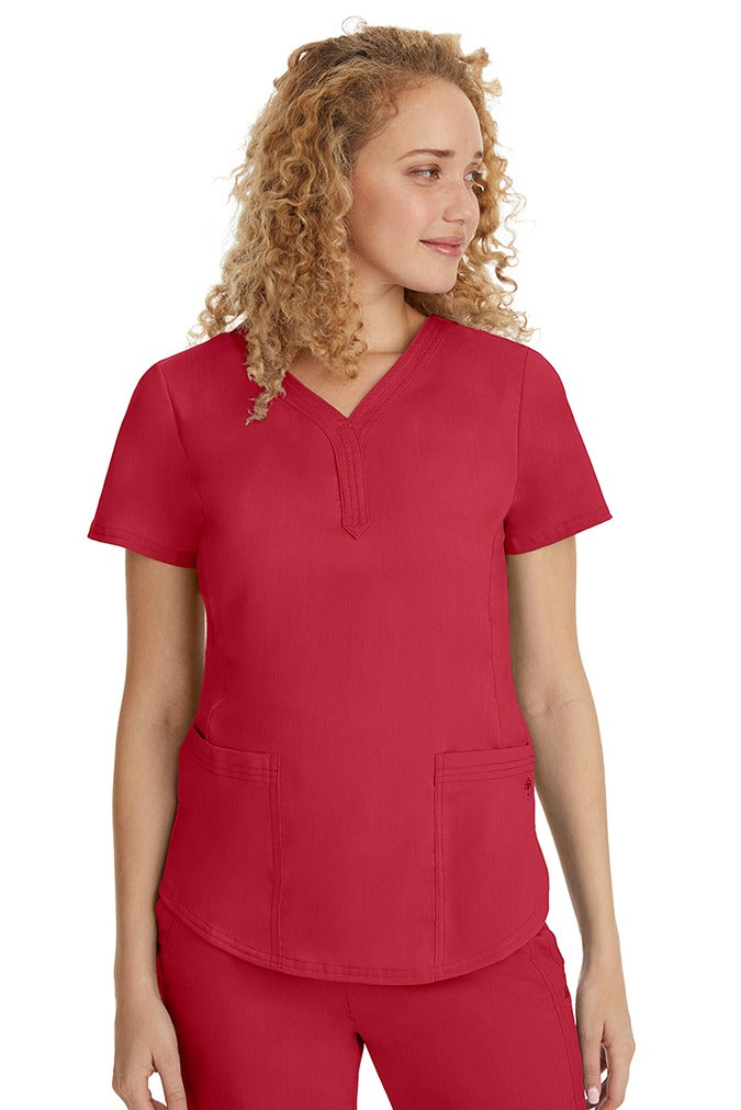 A young female healthcare professional wearing a Purple Label Women's Jane V-Neck Scrub Top in Red featuring 2 front patch pockets.