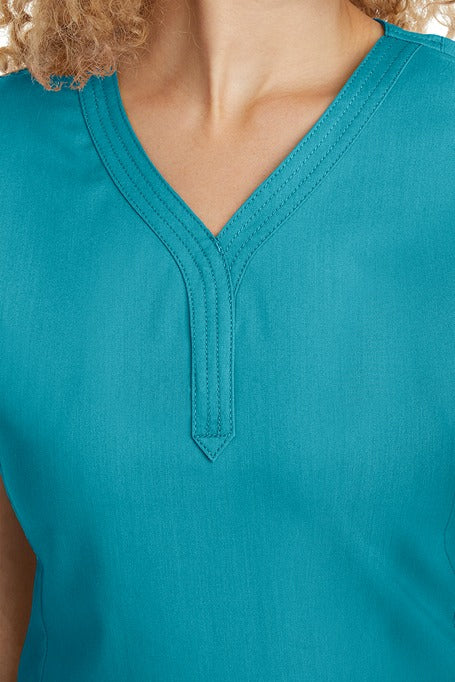A young woman CNA wearing a Women's Jane V-Neck Scrub Top from Purple Label by Healing Hands in Teal featuring triple stitch detail at the neckline.
