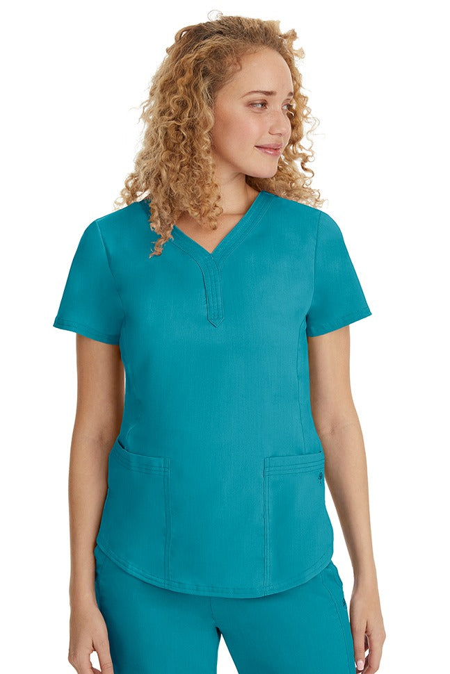 A young female healthcare professional wearing a Purple Label Women's Jane V-Neck Scrub Top in Teal featuring 2 front patch pockets.