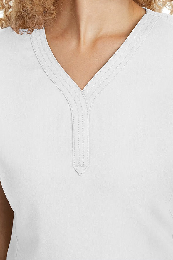 A young woman CNA wearing a Women's Jane V-Neck Scrub Top from Purple Label by Healing Hands in White featuring triple stitch detail at the neckline.