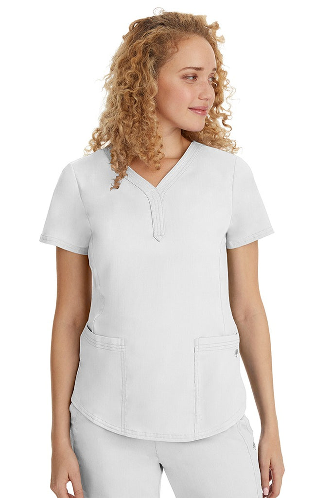 A young female healthcare professional wearing a Purple Label Women's Jane V-Neck Scrub Top in White featuring 2 front patch pockets.