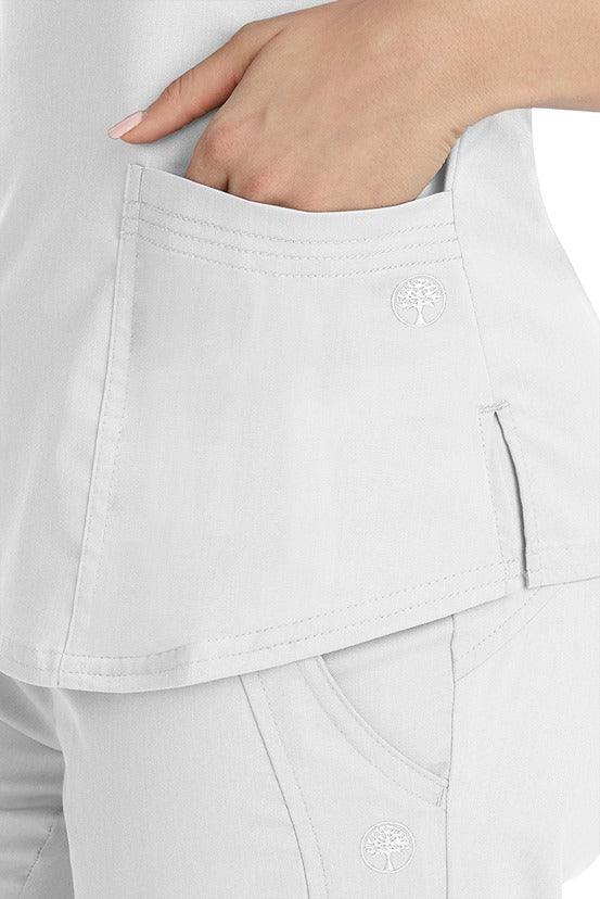 A female healthcare worker wearing a Purple Label Women's Jane V-Neck Scrub Top in White featuring triple needle stitch detail at the pockets.
