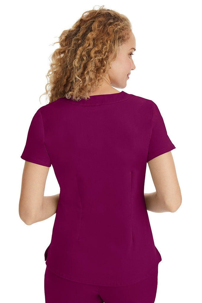 A young LPN wearing a Purple Label Women's Jane V-Neck Scrub Top in Wine featuring a medium center back length of 26.5".