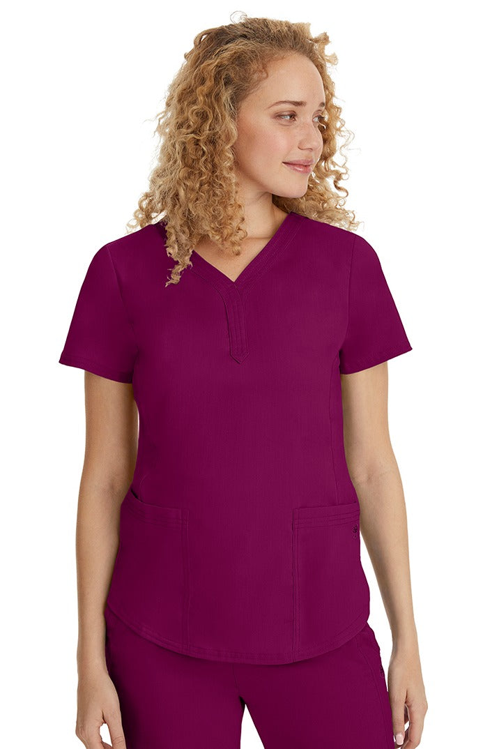 A young female healthcare professional wearing a Purple Label Women's Jane V-Neck Scrub Top in Wine featuring 2 front patch pockets.