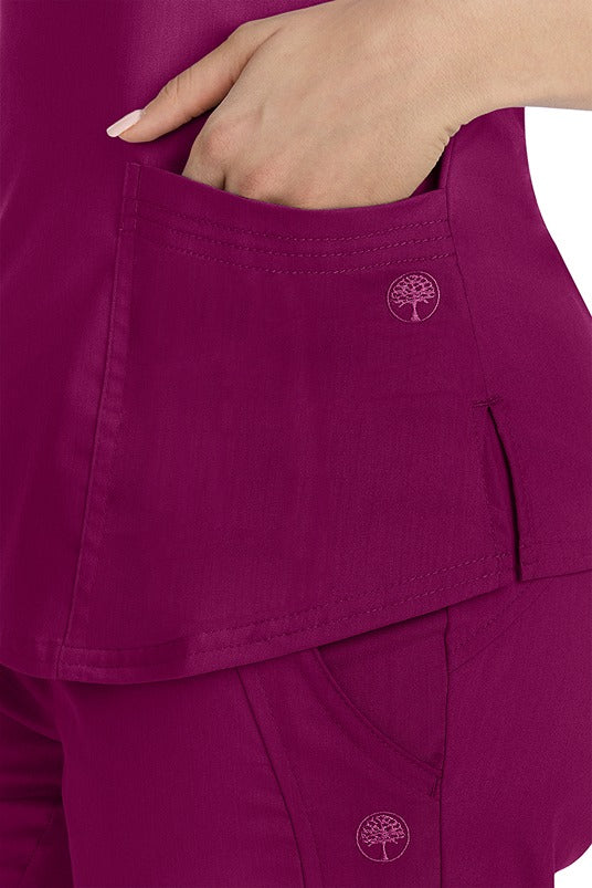 A female healthcare worker wearing a Purple Label Women's Jane V-Neck Scrub Top in Wine featuring triple needle stitch detail at the pockets.
