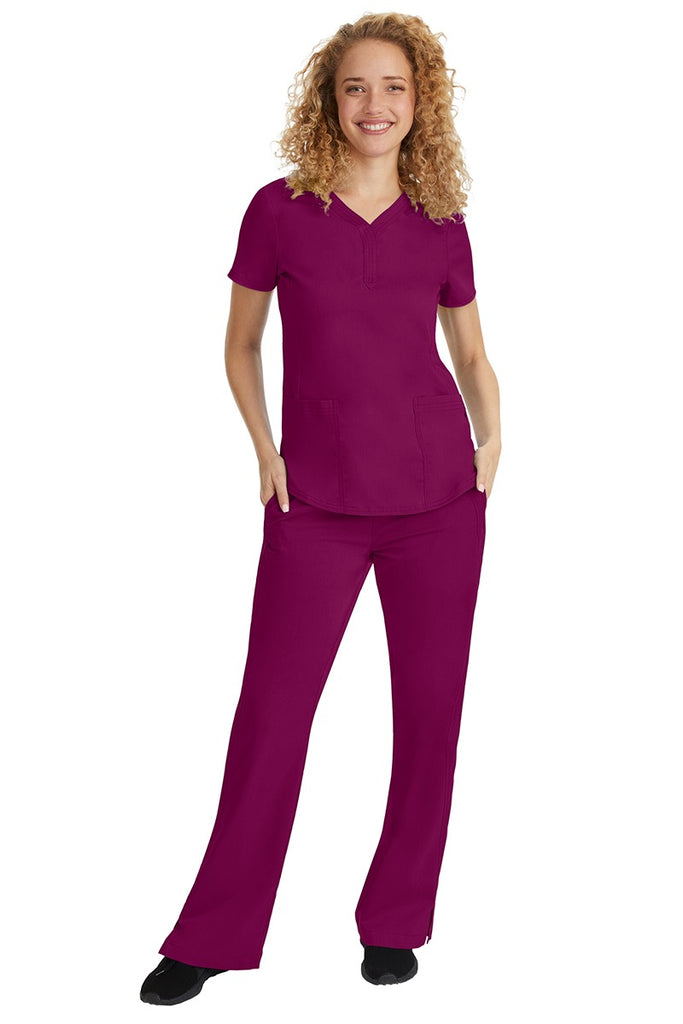 A young female nurse wearing a Purple Label Women's Jane V-Neck Scrub Top in Wine featuring a V-neckline & short sleeves.