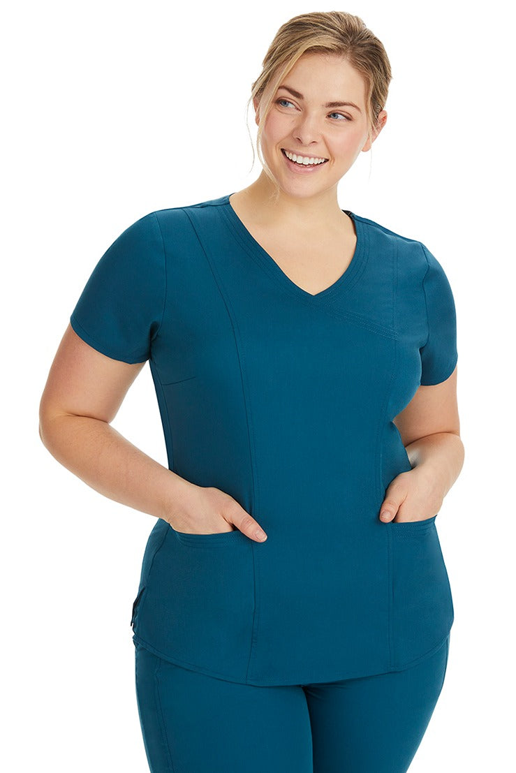 A lady nurse wearing the Purple Label Women's Jordan Crossover Scrub Top in Caribbean featuring side seam vents & side slits for increased breathability & range of motion.