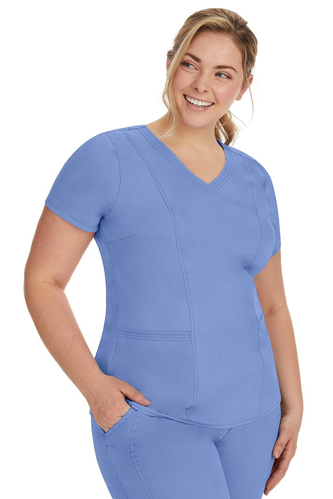 A lady nurse wearing the Purple Label Women's Jordan Crossover Scrub Top in Ceil featuring side seam vents & side slits for increased breathability & range of motion.