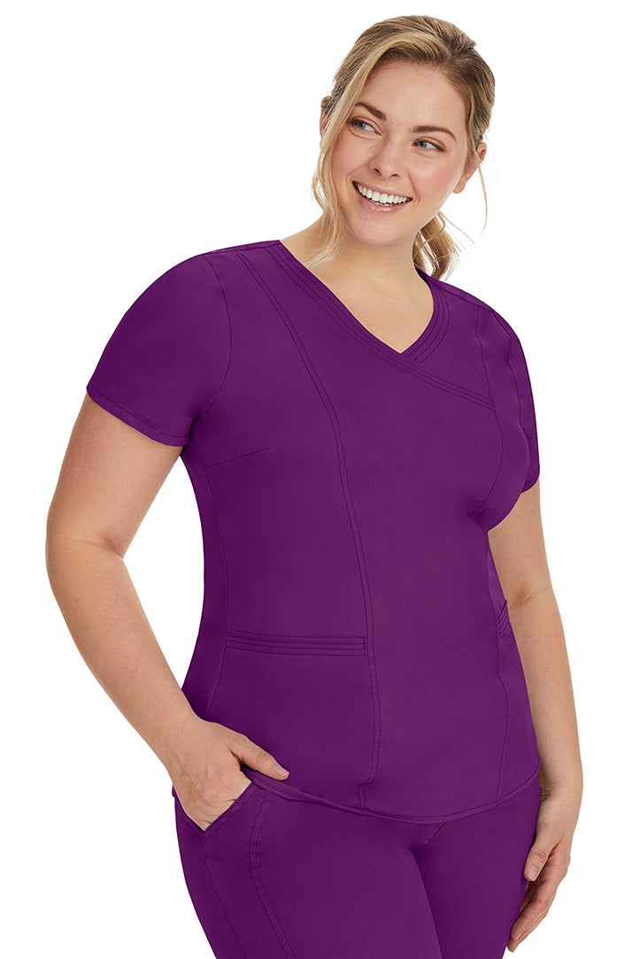 A lady nurse wearing the Purple Label Women's Jordan Crossover Scrub Top in Eggplant featuring side seam vents & side slits for increased breathability & range of motion.