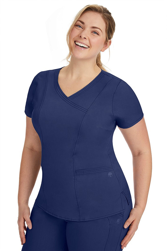 A frontward facing image of a young woman wearing a Purple Label Women's Jordan Crossover Scrub Top in Navy featuring front darts.