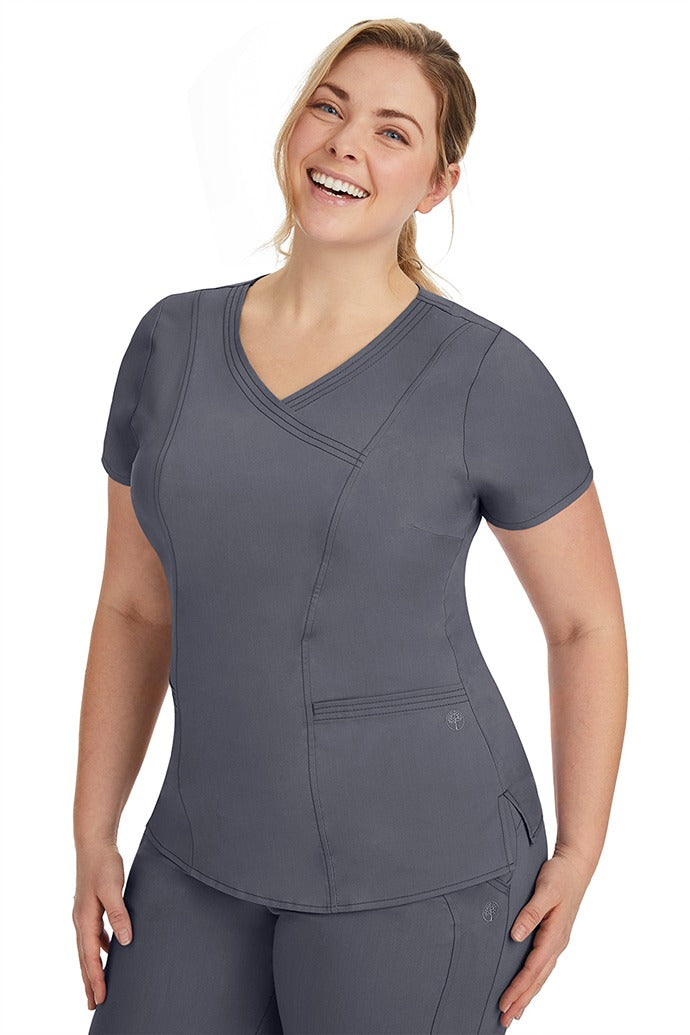 A frontward facing image of a young woman wearing a Purple Label Women's Jordan Crossover Scrub Top in Pewter featuring front darts.