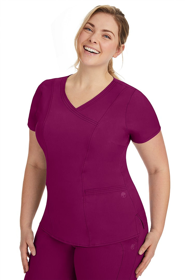 A frontward facing image of a young woman wearing a Purple Label Women's Jordan Crossover Scrub Top in Wine featuring front darts.
