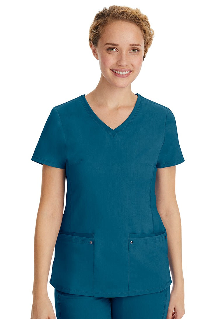 A young LPN wearing a Purple Label Women's Juliet Yoga Scrub Top in Caribbean featuring 2 front patch pockets.