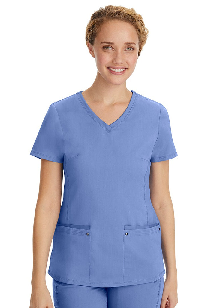 A young LPN wearing a Purple Label Women's Juliet Yoga Scrub Top in Ceil featuring 2 front patch pockets.