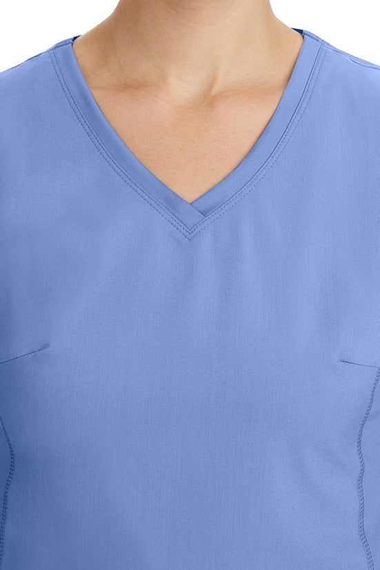 A young healthcare professional wearing a Purple Label Women's Juliet Yoga Scrub Top in Ceil featuring a modern fit.
