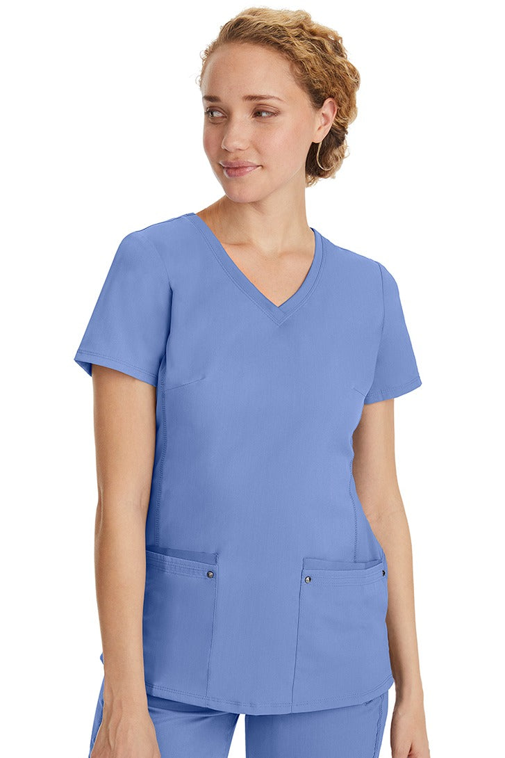 A female healthcare professional wearing a Women's Juliet Yoga Scrub Top from Purple Label in Ceil featuring a side stretch panels.