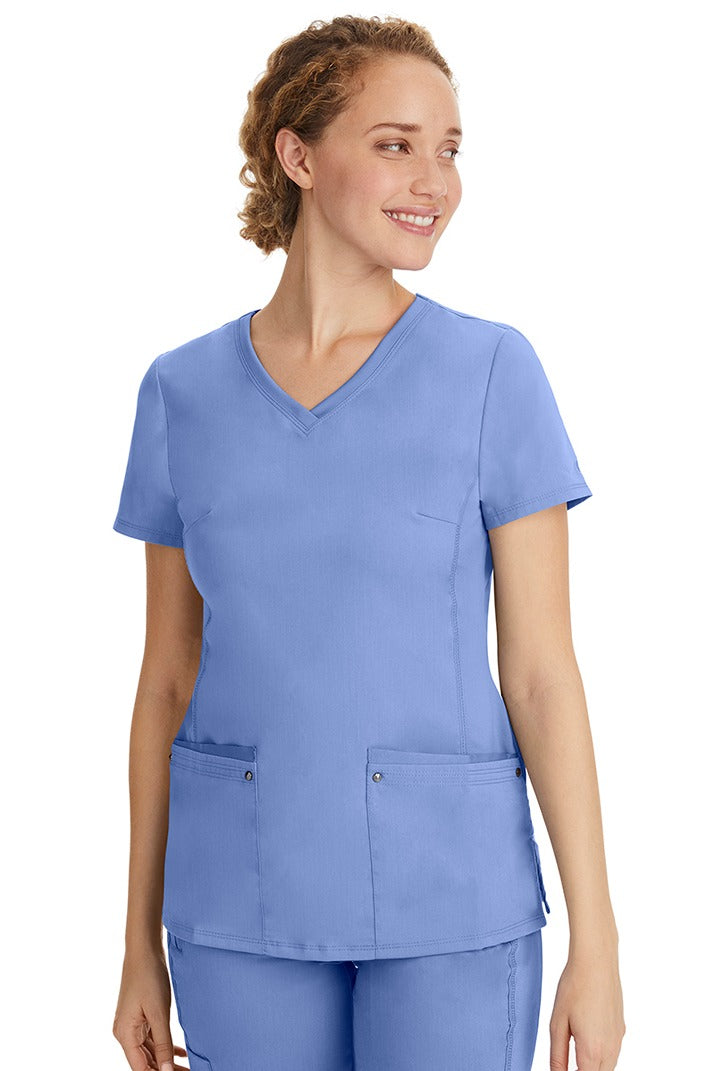 A lady nurse wearing a Purple Label Women's Juliet Yoga Scrub Top in Ceil featuring a super comfortable stretch fabric made of 77% polyester/20% rayon/3% spandex.