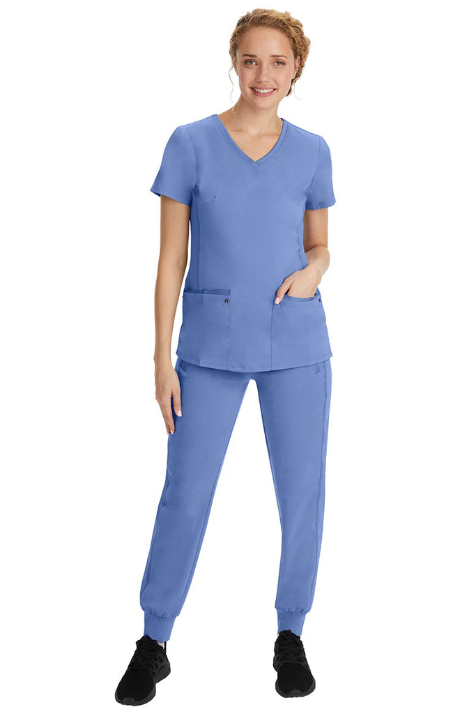 A young female nurse wearing a Purple Label Women's Juliet Yoga Scrub Top by Healing Hands in Ceil featuring a v-neckline.