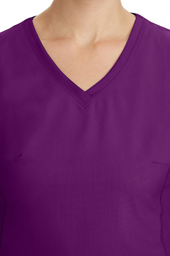 A young healthcare professional wearing a Purple Label Women's Juliet Yoga Scrub Top in Eggplant featuring a modern fit.