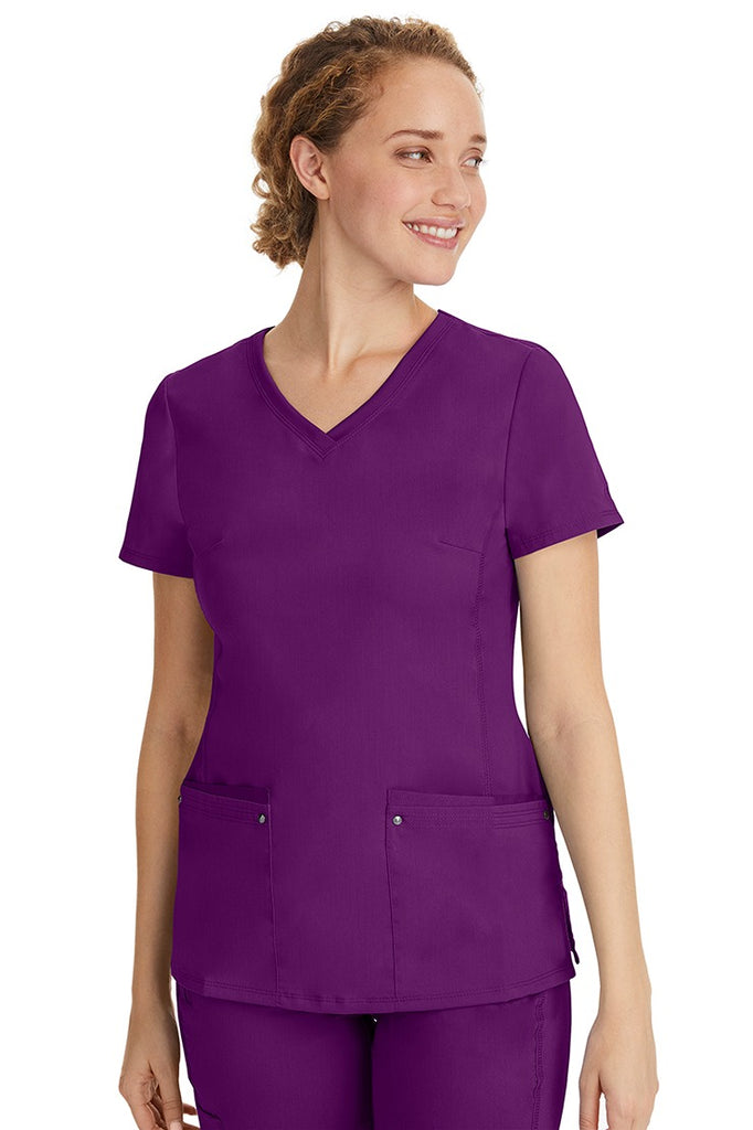 A female healthcare professional wearing a Women's Juliet Yoga Scrub Top from Purple Label in Eggplant featuring a side stretch panels.