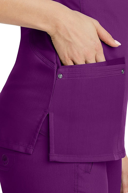 A young woman wearing a Women's Juliet Yoga Scrub Top from Purple Label by Healing Hands in Eggplant  featuring side slits for additional range of motion.