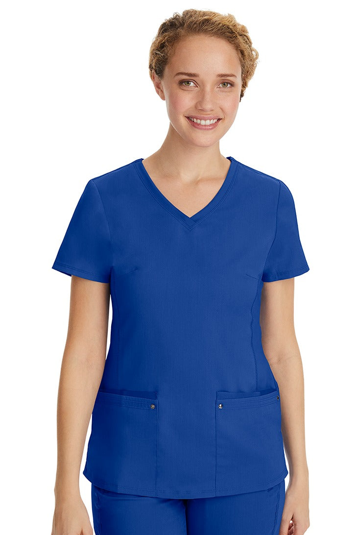 A young LPN wearing a Purple Label Women's Juliet Yoga Scrub Top in Galaxy Blue  featuring 2 front patch pockets.