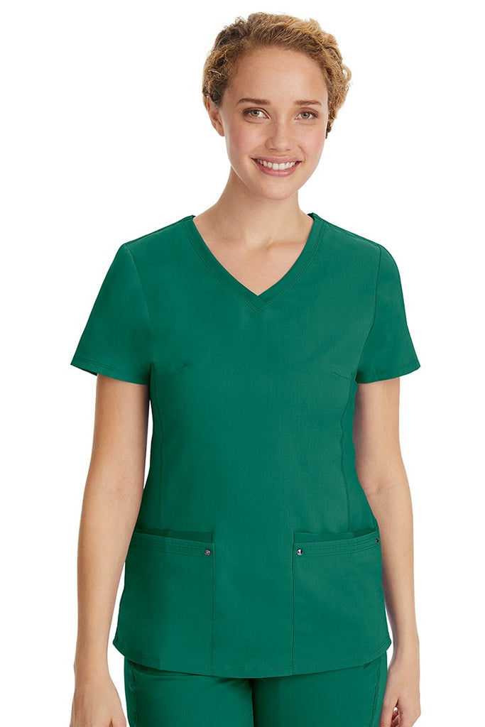 A young LPN wearing a Purple Label Women's Juliet Yoga Scrub Top in Hunter Green featuring 2 front patch pockets.