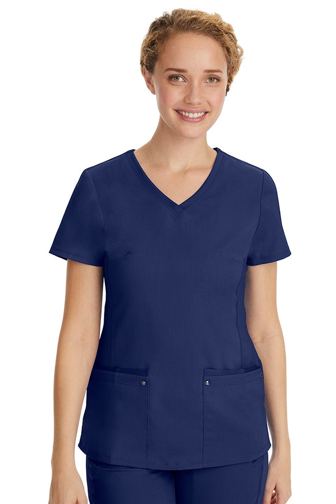 A young LPN wearing a Purple Label Women's Juliet Yoga Scrub Top in Navy featuring 2 front patch pockets.