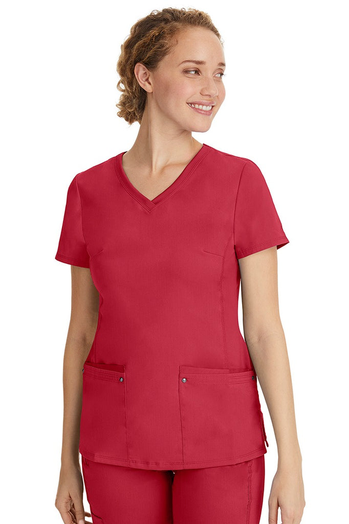 A female healthcare professional wearing a Women's Juliet Yoga Scrub Top from Purple Label in Red featuring a side stretch panels.