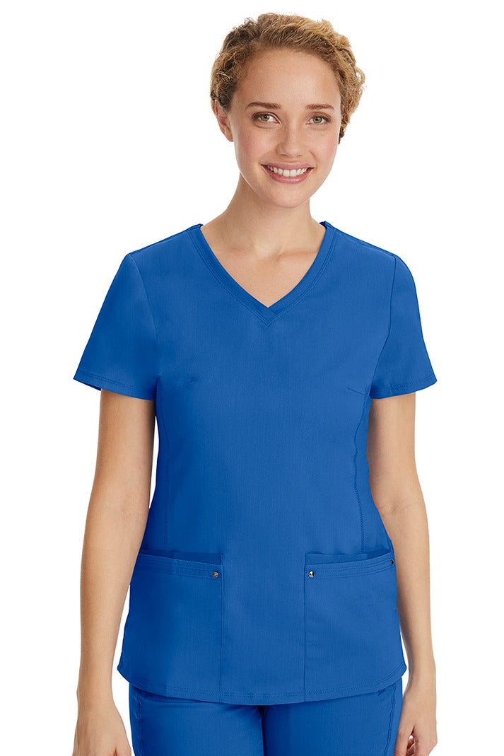 A young LPN wearing a Purple Label Women's Juliet Yoga Scrub Top in Royal featuring 2 front patch pockets.